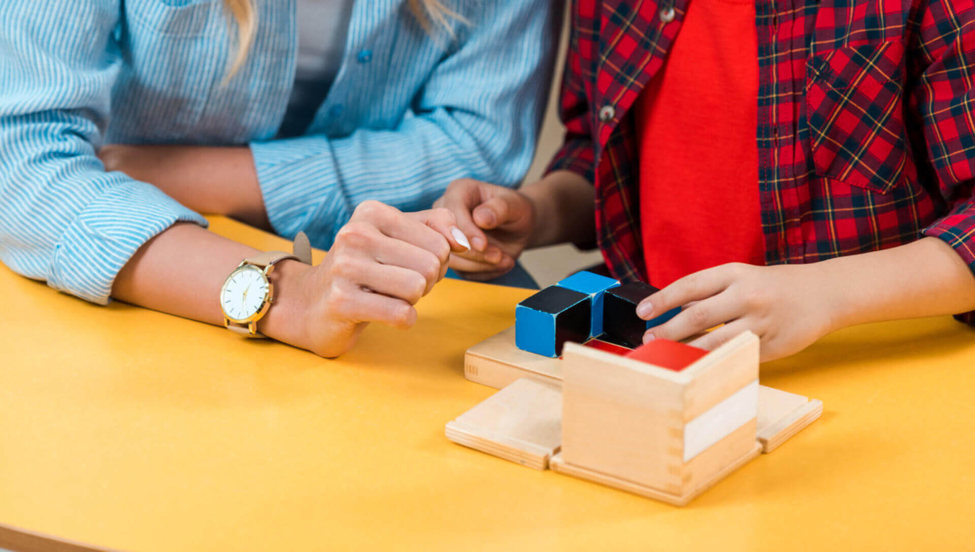 Asian kid playing building blocks by teacher in montessori class