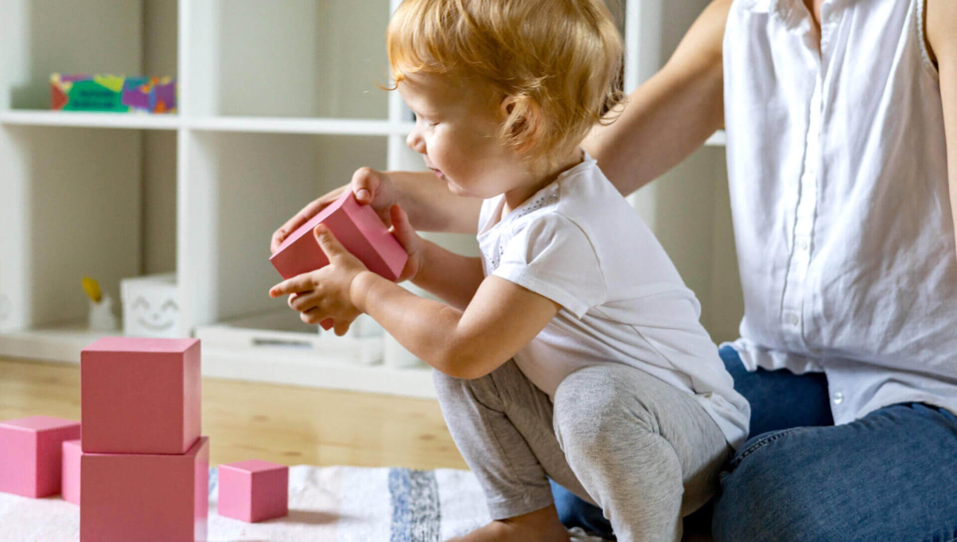 Young mother and little baby assembling pink cube