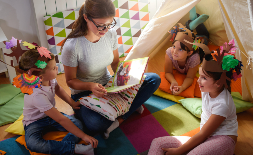Preschool teacher reading a story to children at kindergarten.