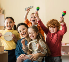 excited multiethnic kids playing musical instruments near happy teacher