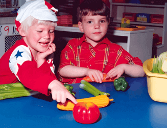 Two young boys sitting at a table with vegetables, preparing a healthy meal together.
